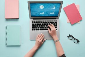 A close-up of a person using a Macbook on a teal table.