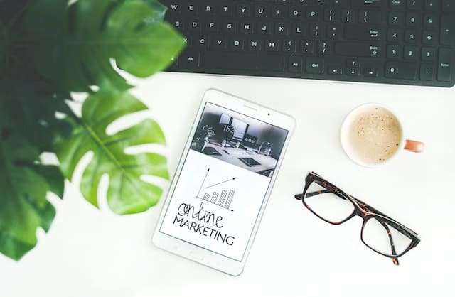 A tablet next to a cup of coffee and a pair of glasses on a white surface.